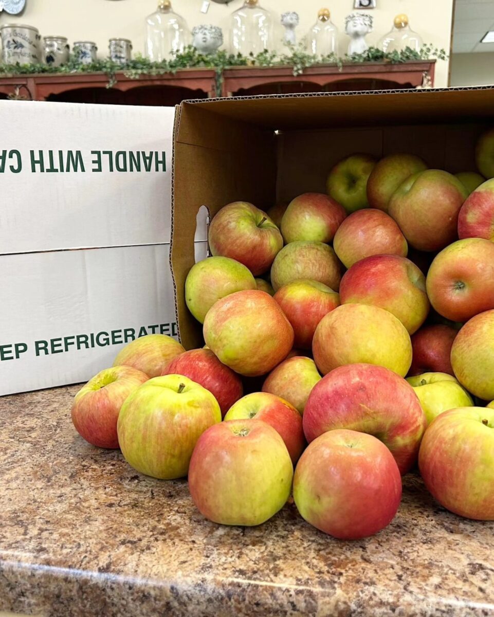 A box of red and green apples spills onto a countertop in a store or market setting.