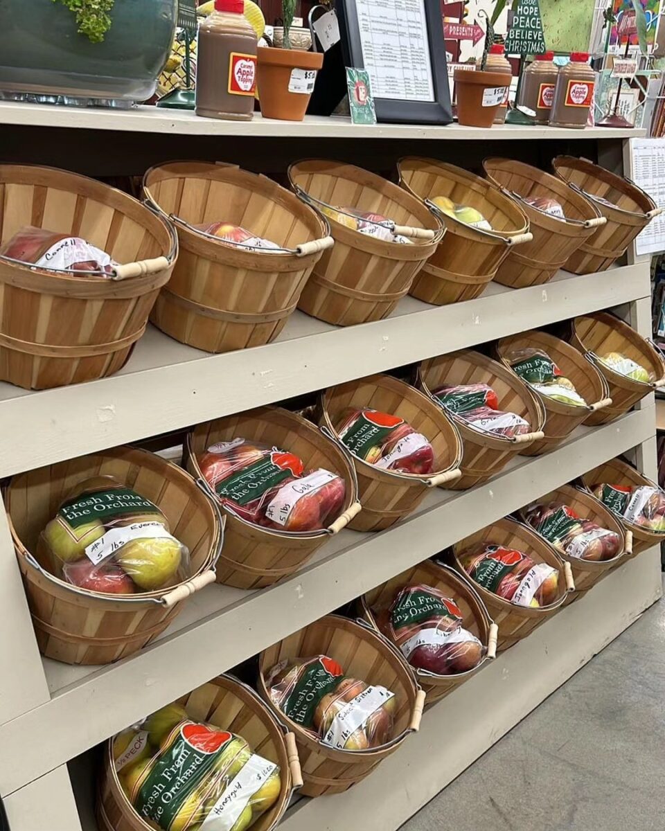 Wooden baskets on a shelf filled with bagged apples in a grocery store produce section.